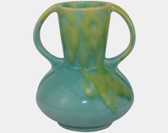 May include: A turquoise ceramic vase with two curved handles. The vase has a rounded base and a cylindrical neck. The top and the inside of the vase are a yellow-green color, with the color dripping down the sides. The vase is a decorative item.