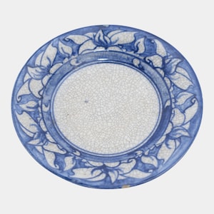 May include: Round ceramic plate with a blue floral design around the rim. The plate has a white center with a cracked, textured appearance. The blue floral pattern is stylized and adds a decorative element to the plate.