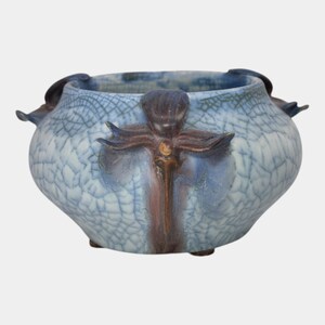 May include: A blue and brown ceramic bowl with a textured, crackled pattern. The bowl has a rounded shape with decorative handles and a central, stylized floral design. The color palette includes shades of blue, brown, and a touch of gold.