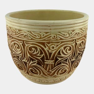 May include: A beige ceramic bowl with intricate, raised brown floral and scrollwork designs. The rim and base feature a lighter beige color, creating a contrast with the darker, detailed patterns. This decorative bowl is suitable for home decor.