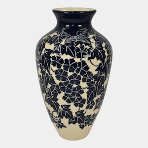 May include: A navy blue and cream-colored ceramic vase. The vase features a floral and leaf pattern in navy blue against a cream background. The rim and top portion of the vase are navy blue.