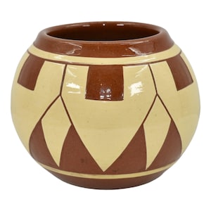 May include: A round ceramic vase with a geometric pattern. The vase features a cream-colored base with a repeating pattern of brown shapes. The rim and interior are also brown. The vase has a wide opening and a rounded body.
