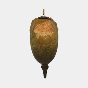 May include: An acorn-shaped ornament with a textured, mottled surface in shades of green and brown. A leaf design is visible on the upper portion. The ornament has a dark brown cap and a gold-colored string for hanging. A decorative item.
