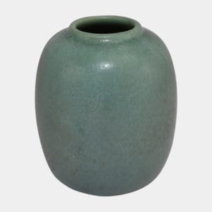 May include: A small, rounded, celadon-colored ceramic vase. The vase has a narrow opening and a smooth, slightly textured surface. The overall shape is oval, with a subtle, matte finish. This decorative vase is suitable for home decor.