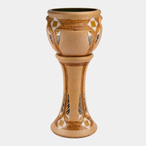 May include: A tan ceramic planter on a pedestal. The planter has a rounded top with a dark green interior and is decorated with geometric patterns in yellow, white, and blue. The pedestal has a flared base and a textured surface.