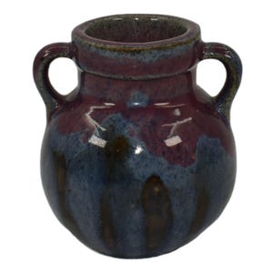 May include: A small, ceramic vase with two handles. The vase has a rounded body and a wide opening. The exterior features a blend of blue and purple hues, with a darker shade at the base and a lighter shade towards the top.