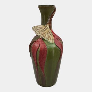 May include: A green ceramic vase with red leaf accents and a cream-colored moth. The vase has a slender neck and a bulbous body. The moth is perched on the leaves, adding a touch of nature-inspired artistry.