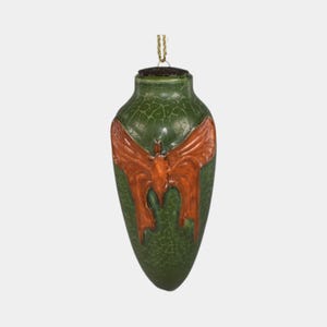 May include: Green, vase-shaped ornament with a textured surface and a bronze-colored butterfly design. The ornament has a gold-colored string for hanging. The butterfly is centered on the front of the ornament.