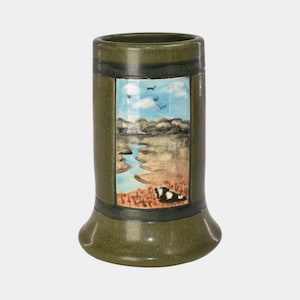 May include: A green ceramic vase with a landscape painting. The painting depicts a river scene with a blue sky, clouds, and birds. The vase has a flared base and a cylindrical body.