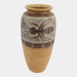 May include: A ceramic vase featuring a tan speckled base and a light gray upper section. The upper portion displays a dark brown embossed ant illustration, framed by decorative geometric bands in brown and tan around the neck and middle.