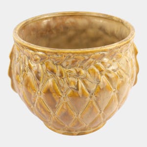 May include: A round, glazed ceramic planter in shades of yellow and brown. The planter features a quilted diamond pattern and decorative leaf-like accents around the rim. The interior is a darker brown.
