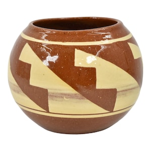 May include: A brown ceramic pot with a geometric pattern of white arrows. The pot is round and has a wide opening.