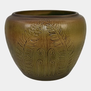 May include: A round ceramic planter with a wide opening and a tapered base. The exterior features a matte olive green glaze with a darker brown gradient near the rim and base. Embossed fern leaf patterns and curled frond motifs decorate the surface.