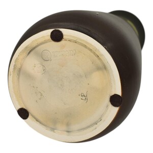 May include: A brown ceramic vase with a white base and a dark brown exterior. The base has three small, round, black pads. The bottom of the vase has the text "EPHRAIM" and the number "27".