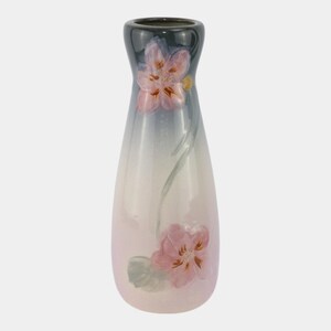 May include: A decorative ceramic vase with a slender, elongated shape. The vase features a gradient color scheme, transitioning from a dark green rim to a soft pink base. Pink floral designs are painted on the vase, adding a touch of elegance.
