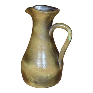 May include: A brown ceramic pitcher with a wide mouth and a handle. The pitcher has a mottled glaze with a greenish hue.