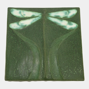 May include: Square ceramic tile with a dragonfly design. The dragonfly has light green wings and a dark green body, set against a textured dark green background. The tile features a raised relief of the dragonfly and plant-like elements.
