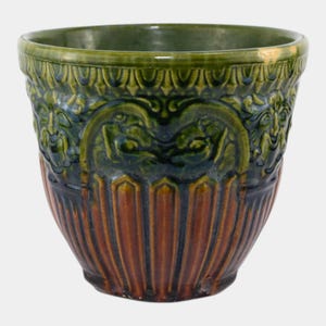 May include: A ceramic planter with a detailed design. The top rim is green, transitioning to a dark green and brown body. The planter features a repeating pattern of vertical lines and ornate relief details, creating a textured appearance. The planter is suitable for indoor or outdoor use.