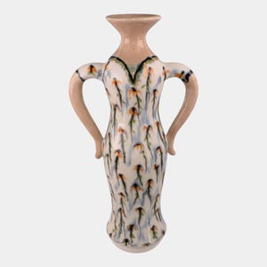 May include: A ceramic vase with a cream-colored base and a light tan neck. The vase features two curved handles and is decorated with a floral pattern in orange, blue, and green on a white background. The vase is approximately 10 inches tall.
