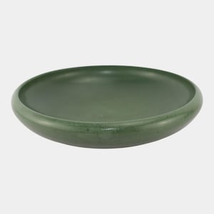 May include: A round, dark green ceramic bowl with a slightly raised rim. The bowl has a smooth, matte finish and a shallow interior. The overall design is simple and modern, suitable for serving or display.