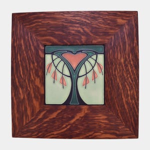 May include: Square wooden framed tile with an art nouveau design. The tile features a stylized tree with a heart-shaped top in shades of green, coral, and black against a light green background. The frame is made of dark brown wood.