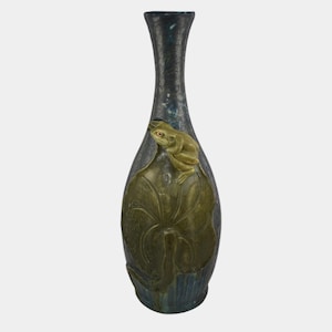 May include: A tall, dark blue vase with a textured surface and a frog and lily pad design. The frog is light green with red eyes, and the lily pad is a darker green. The vase has a narrow neck and a wide base.