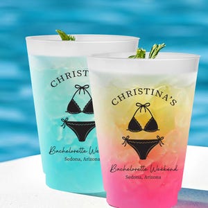 May include: Two plastic cups with colorful drinks, one blue and one gradient of yellow and pink. Each cup has a black bikini graphic and text that reads "Christina's Bachelorette Weekend, Sedona, Arizona."