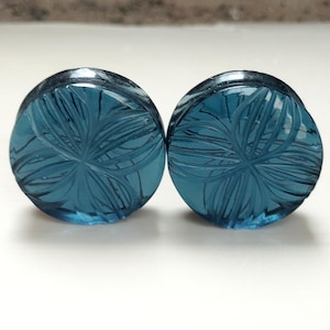 Könnte beinhalten: Ein Paar blaue Glas-Ohrmanschetten mit einem geschnitzten Blumenmuster.