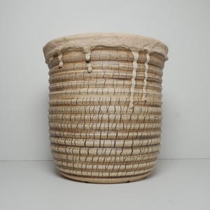 May include: A cylindrical ceramic vessel featuring a textured, ribbed exterior with a beige and brown crackle glaze finish. The top rim is adorned with a thick, light-colored glaze that drips down the sides, creating a layered, tactile appearance.