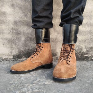 May include: Brown suede boots with black leather accents and laces. The boots have a chunky heel and a rounded toe.