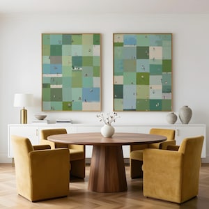 May include: Two large rectangular wall art pieces featuring a grid of green, blue, and beige squares with small figures, displayed above a round wooden dining table with four mustard yellow upholstered chairs in a bright room.