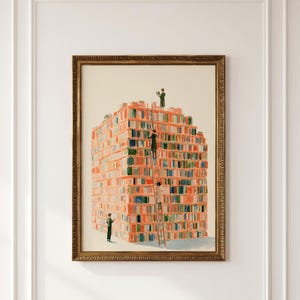 May include: A framed wall art print depicting a large, rectangular stack of books in shades of orange, red, and green. Four small figures are positioned around the stack, with three climbing a tall wooden ladder to reach the top of the book pile.