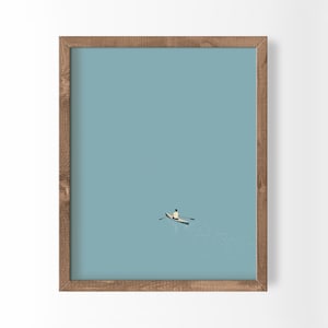 Op de afbeelding: Een ingelijste wandkunstprint met een kleine boot met één roeiende persoon, geplaatst in het midden onderaan tegen een effen lichtblauwe achtergrond. De lijst is gemaakt van middelbruin hout met een zichtbare houtnerf en rechthoekig.