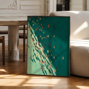 May include: A rectangular framed wall art print featuring a high-angle view of a crowd of small, stylised figures in various colours walking across a teal and green surface, casting long, dark shadows that stretch across the composition.
