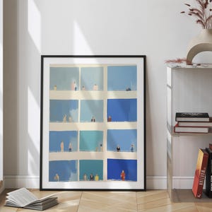 a framed collage of blue squares with various people in different poses, placed on a wooden floor next to a bookshelf.