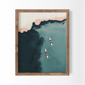 Op de afbeelding: Een ingelijste kunstdruk met een luchtfoto van twee witte kajaks op diepblauw en groenblauw water. De compositie bevat een zandkleurige kustlijn aan de bovenkant, die contrasteert met de donkere, kolkende diepten van het oceaanwater eronder.