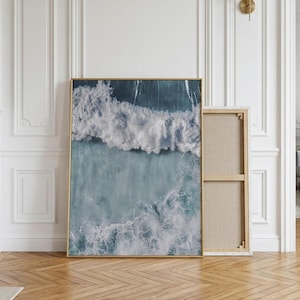 Peut inclure: Une impression d'art murale rectangulaire présentant une vue aérienne de vagues océaniques s'écrasant sur le rivage. L'image affiche des nuances d'eau bleu profond et turquoise avec des motifs d'écume blanche. Le cadre est en métal doré fin.