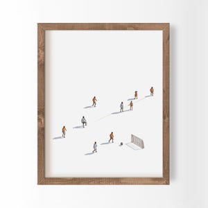 May include: A framed art print featuring a minimalist white background with several small figures of football players in orange and white uniforms, a football, and a goal net, all arranged in a sparse, scattered composition on the white field.