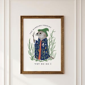 May include: A framed wall art print featuring an illustration of an otter wearing a green hat and a blue floral robe, holding a small twig. The text reads THE HORRORS PERSIST YET SO DO I. The otter is surrounded by green seaweed-like foliage.