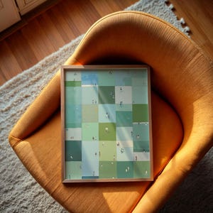 a framed collage of small square images arranged in a grid-like pattern, resting on an orange chair.