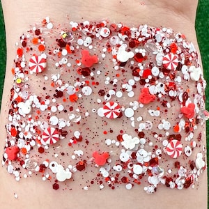 May include: A clear gel with red, white, and clear glitter, candy cane shapes, Mickey Mouse silhouettes, and heart shapes. The glitter and shapes are scattered throughout the gel.