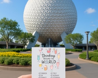 Op de afbeelding: Een kleine kaart met de tekst "Drinking Around the World" en illustraties van verschillende cocktails wordt voor een grote, witte geodetische bol gehouden. De kaart vermeldt landen als Canada, het VK, Frankrijk en Japan.