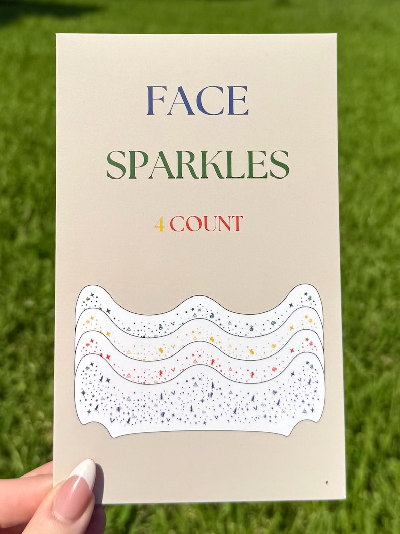 May include: A beige card with the words "FACE SPARKLES 4 COUNT" in blue, green, and red. The card features a wavy design with various colored sparkles and star shapes, perfect for face decoration.