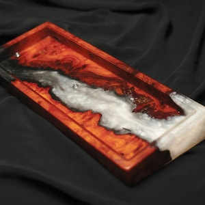 Könnte beinhalten: Ein rechteckiges Holztablett mit einer weißen und schwarzen Harzeinlage. Das Tablett hat eine natürliche Holzoptik und ist perfekt für die Aufbewahrung von kleinen Gegenständen.