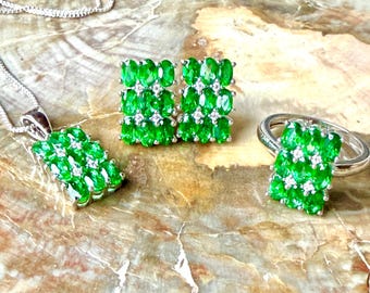 May include: A jewelry set consisting of a pendant necklace, a pair of stud earrings, and a ring. Each piece features a rectangular cluster of oval-cut vibrant green stones accented with small clear stones set in a polished silver-tone metal.