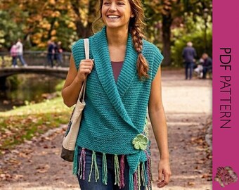 May include: A teal knitted wrap with fringe and a flower accent. The wrap is sleeveless and has a shawl collar. The image shows a person wearing the wrap while walking on a path. The text "PDF PATTERN" is visible on the right side of the image.