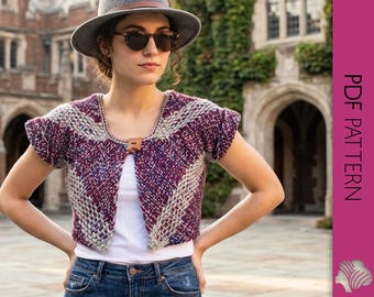 May include: A short-sleeved, open-front knit bolero in shades of purple and cream, fastened with a wooden button. The bolero is worn over a white top and paired with blue jeans. The image also includes a gray hat and sunglasses.