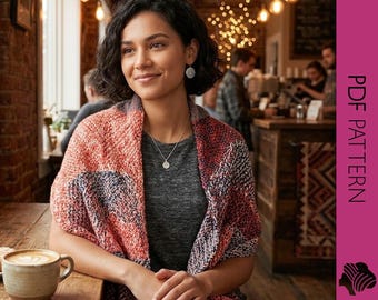 May include: A woman wearing a red, orange, and blue patterned shawl, a gray shirt, and a silver necklace. She is sitting at a wooden table with a cup of coffee and a pastry. The background includes a brick wall and a coffee shop setting.