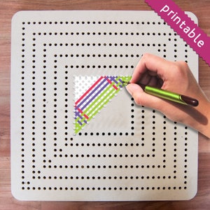 May include: A white pegboard with a grid of holes, used for creating pixel art. A hand is using a green pen to draw a design on the board, which includes green, purple, red, and white lines.