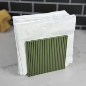 May include: A green, ribbed napkin holder with a stack of white napkins inside.